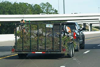 Tampa, Florida, U.S - Nov 10, 2025 - A pickup truck towing an open utility trailer filled with yard debris and landscaping