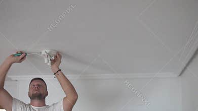 A bearded man attaches a lamp to the ceiling in his apartment