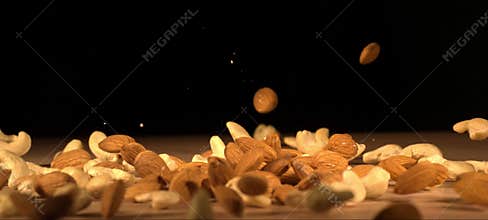 Super slow-motion of almonds and cashews fall on wooden table. Healthy snack, satisfying crunch.