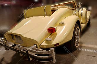 Classic convertible car parked in a garage with bright yellow color and chrome details visible under indoor lighting