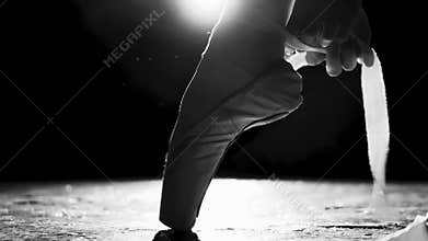 Close up female hands tying pointe shoes on the leg isolated in spotlight on black background. Black and white shot