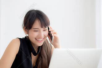 Beautiful young freelance asian woman smiling working on laptop computer and talking mobile smart phone at desk office