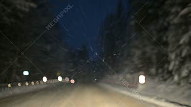 We drive through a winter forest along a snowy road at night. Focus on snow flakes flying in the windshield