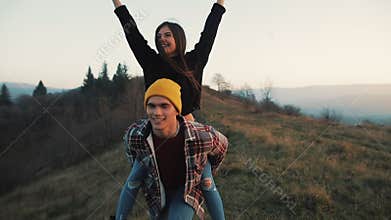 Young couple in love on vacations enjoying mountains. Attractive man is carrying girlfriend on his shoulders and whirls