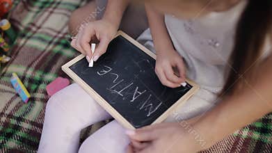 A little girl learns to write words on the blackboard with chalk. Mom teaches daughter to write letters, alphabet