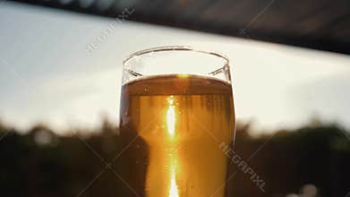 A mug of cold beer against the sky and a yellow sunset in the sun