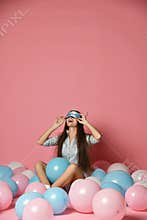Portrait of trendy cheerful young woman having many color air balloons looking up enjoying ballons isolated on pink background.