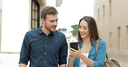Couple walking browsing cellphone in the street