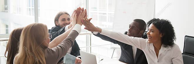 Diverse businesspeople sitting at desk celebrating success giving high five