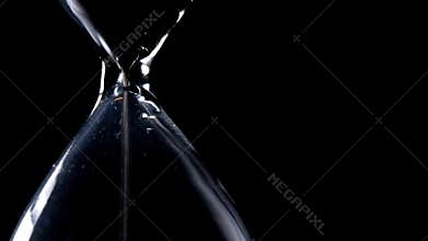 The sand flow in the hourglass with black background and lateral light backlight in lateral composition in loop