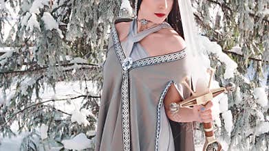 Slim model with long black hair and soft make-up posing for camera, elf princess looks at her reflection in blade of