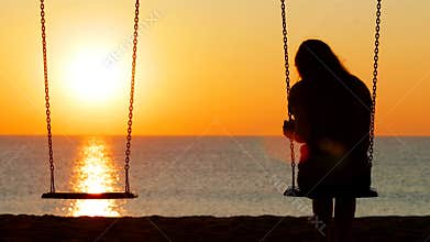 Sad girl swinging at sunset on the beach