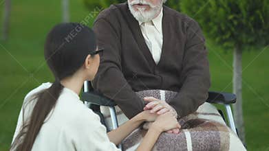 Kind-hearted daughter supporting father in wheelchair during rehabilitation