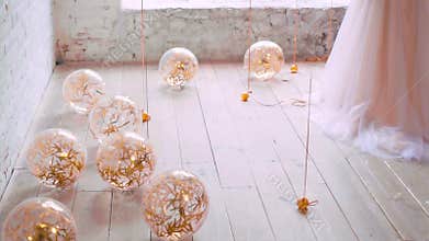 Light bright balloons lie and roll on floor, filled with golden serpentine, glitter in the light of the sun, joyful