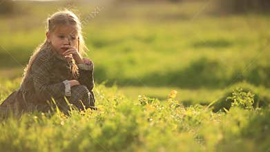 Young sad girl lonely in grass field. A young girl is sitting picking grass alone in a grass field, frustrated or sad