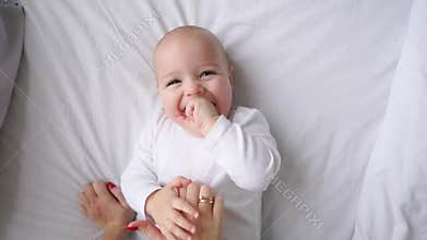 Baby in white t-shirt lying on a white bed and laughing looking at the camera top view slow motion