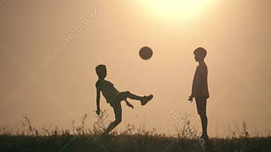Two boys playing soccer at sunset. Silhouette of children playing with a ball at sunset. The concept of a happy family