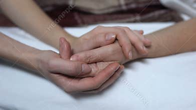 Warm daughters hands stroking and calming down sick mother in bed, assistance