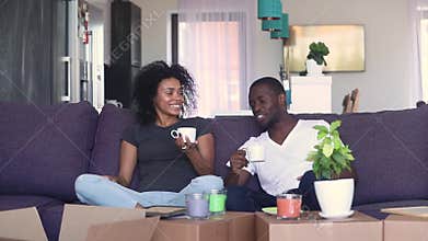 Happy african couple drinking coffee unpacking boxes in new home