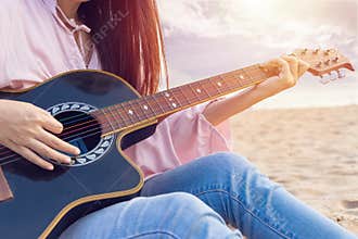 Woman`s hands playing acoustic guitar, capture chords by finger on sandy beach at sunset time. playing music concept