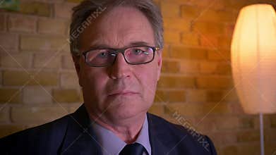 Portrait of senior businessman in formal costume watching into camera being serious in cozy home background.