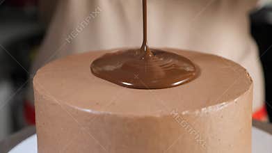 Pastry chef pours liquid chocolate on the top of the cake to decorate it.