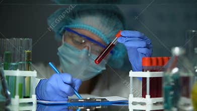 Scientist checking tube with blood analysis and making notes, epidemic outbreak