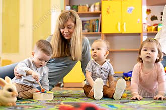 Nursery teacher looking after children in daycare. Little kids toddlers play together with developmental toys.