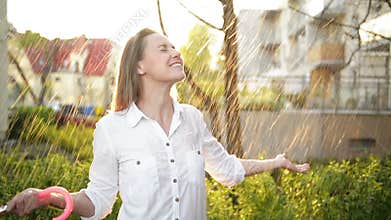 Waist Up Portrait Of Cheerful Girl Holding Umbrella And Catching Rain Drops With Smile. She is Stretching Hand And
