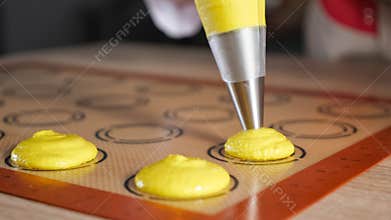 Pastry chef is cooking macaroons. Pouring dough on stencil silicone mat.