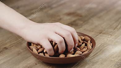 Woman Picks Up a handful of almonds, To Eat, From Her Bowl. took a nut on the left side