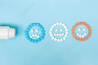 Multicolored pills and funny faces and a plastic bottle on a blue background. The concept of antidepressants and healing