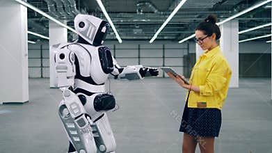 Girl with tablet controls a cyborg, typing on its panel.