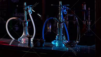 Two hookahs stand on the bar counter in a hookah bar in the dark.