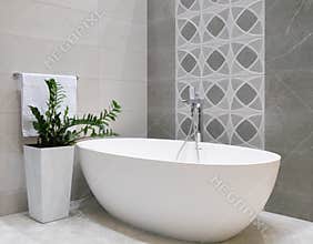 Modern bathroom interior design with white stone bathtub, grey tiles wall, ceramic flowerpot with green plant and hanger with