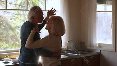 Happy mature senior couple dancing laughing in the kitchen