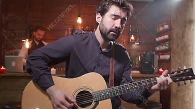 Young handsome guitar player performs a song in a bar
