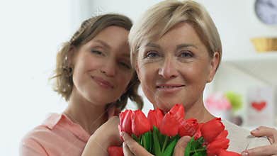 Portrait of adult daughter and mother holding tulips, celebrating Women Day