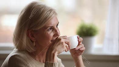 Dreamy happy middle aged woman looking away drinking morning coffee