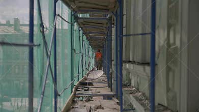 Two male workers in uniform and helmet walk along long blue metallic scaffolding