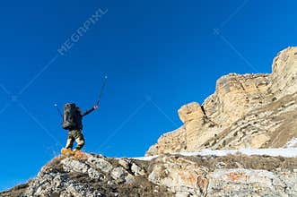 Hiker hipster with a large backpack at the foot of the epic rocks declares intention to win.