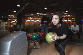 Beautiful young girl playing bowling. Woman with ball for bowling in hands in motion