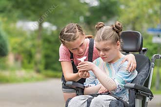 Disability a disabled child in a wheelchair relaxing outside with her sister