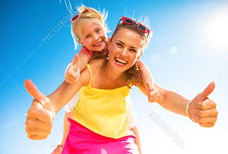 Smiling trendy mother and child on beach showing thumbs up
