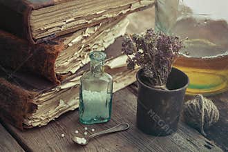 Stack of old books, vintage mortar of medicinal herbs, vial of h