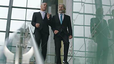 Two corporate executives chatting while descending stairs in company.