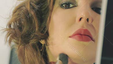 Young woman applying makeup in the mirror close-up