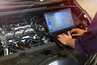 Mechanic Using Laptop While Examining Car Engine