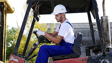 Forklift truck driver in a factory or warehouse driving between rows of shelving with stacks of boxes and packaging