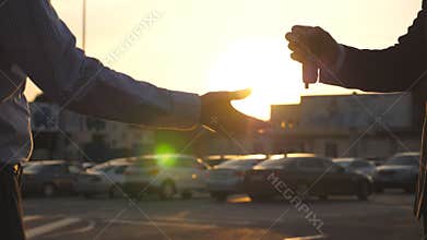 Male hands of dealer giving keys of car to client with sun flare at background. Arm of businessman passed car key